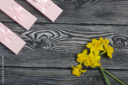 Fototapeta Naklejka Na Ścianę i Meble -  A bouquet of yellow daffodils lies on the surface of brushed pine boards. Near cardboard boxes with gifts. Pink and lilac, decorated with ribbon bows.