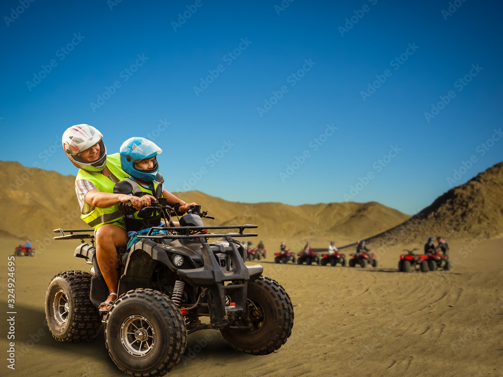 The joyful young family sitting on the ATVs in the desert