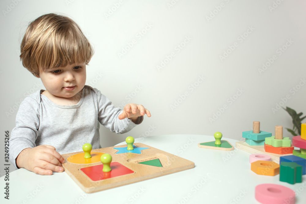 Beautiful toddler play with a wooden frame puzzle geometric figure toys at home. Toddler play with a color educational toy. Child play at the table in the baby room. Child development. Funny baby. Beautiful toddler play with a wooden frame puzzle geometric figure toys at home. Toddler play with a color educational toy. Child play at the table in the baby room. Child development. Funny baby.