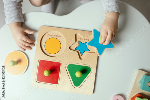 Beautiful toddler play with a wooden frame puzzle geometric figure toys at home. Toddler play with a color educational toy. Child development. Baby hands. View from above. Detail.