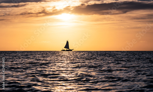 Silhouette of a lonely sailboat on the horizon during colorful sunset on the Caraibbean Sea off the shores of Caye Caulker, Belize. © Maritxu22