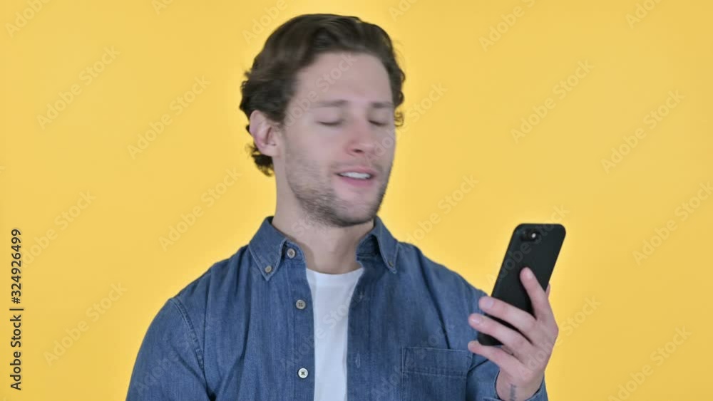 Young Man with Loss on Smartphone, Failure on Yellow Background Young Man with Loss on Smartphone, Failure on Yellow Background