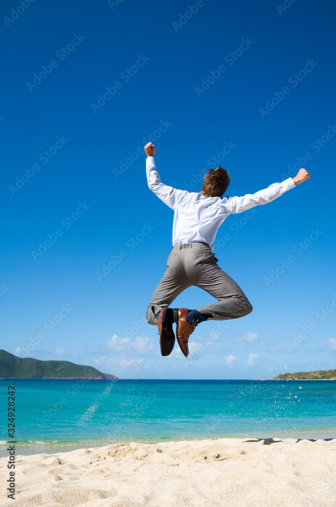 Businessman jumping into the air above a tropical beach clicking his heels together in celebration Businessman jumping into the air above a tropical beach clicking his heels together in celebration