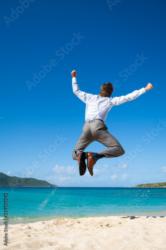 Businessman jumping into the air above a tropical beach clicking his heels together in celebration