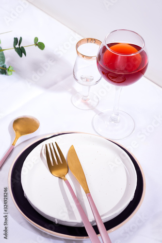 Tableware and decorations for serving a festive table. Plates, red wine glass and cutlery on white textile background.