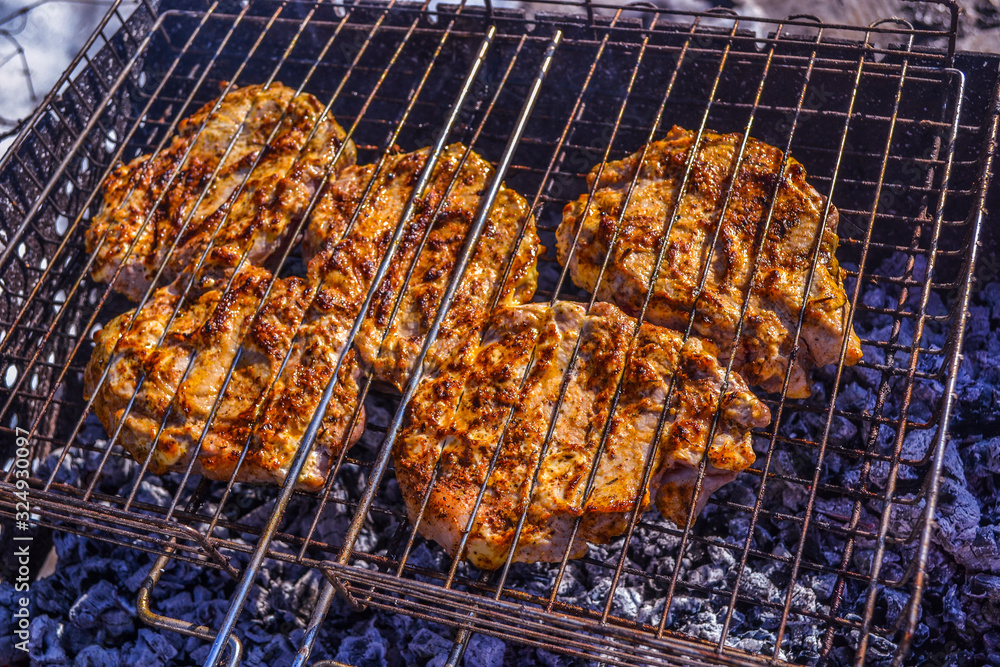 Grilled meat in barbecue with flames and coals. Grilled meat concept.  Few pieces of slightly burnt meat on charred grate with fire and smoke below.  Frying pork on a skewer over a brazier.