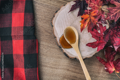 Slika na platnu Maple syrup in wooden spoon top view over dining table wood log