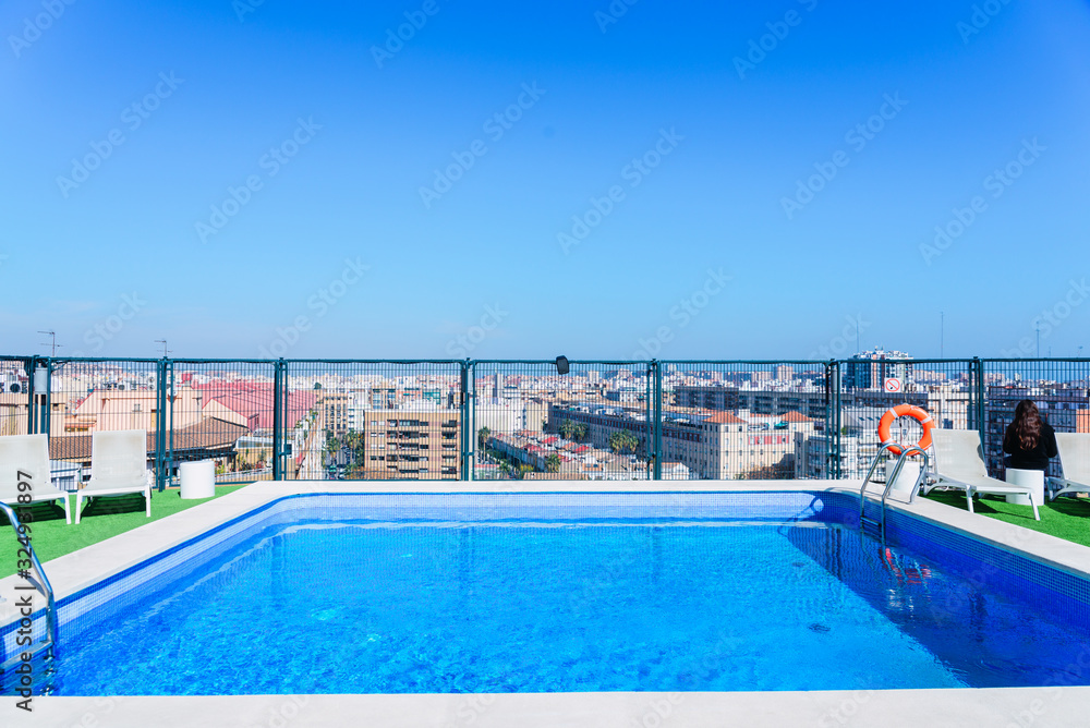 A swimming pool with sun beds on the roof of a building in the city.