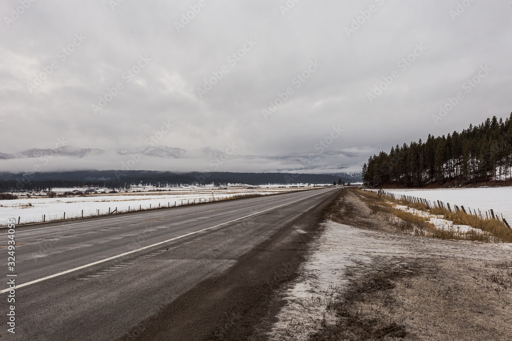 Empty highway in cold of winter with fog shrouded mountains and trees on overcast day
