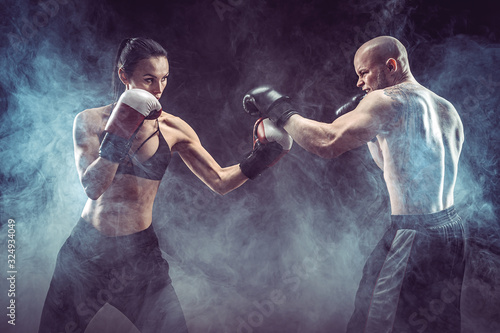 Fototapeta Naklejka Na Ścianę i Meble -  Shirtless Woman exercising with trainer at boxing and self defense lesson, studio, smoke on background. Female and male fight,