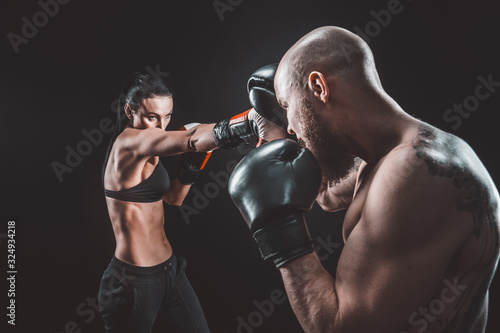 Shirtless Woman exercising with trainer at boxing and self defense lesson, studio, smoke on background. Female and male fight, © zamuruev