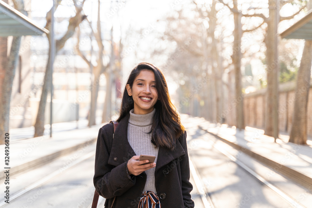Portrait of smiling young woman with smartphone on tram line Portrait of smiling young woman with smartphone on tram line