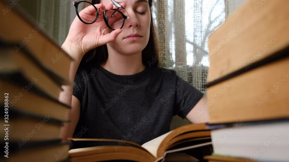 Tired young woman removing glasses, massaging eyes after reading paper book. Female student