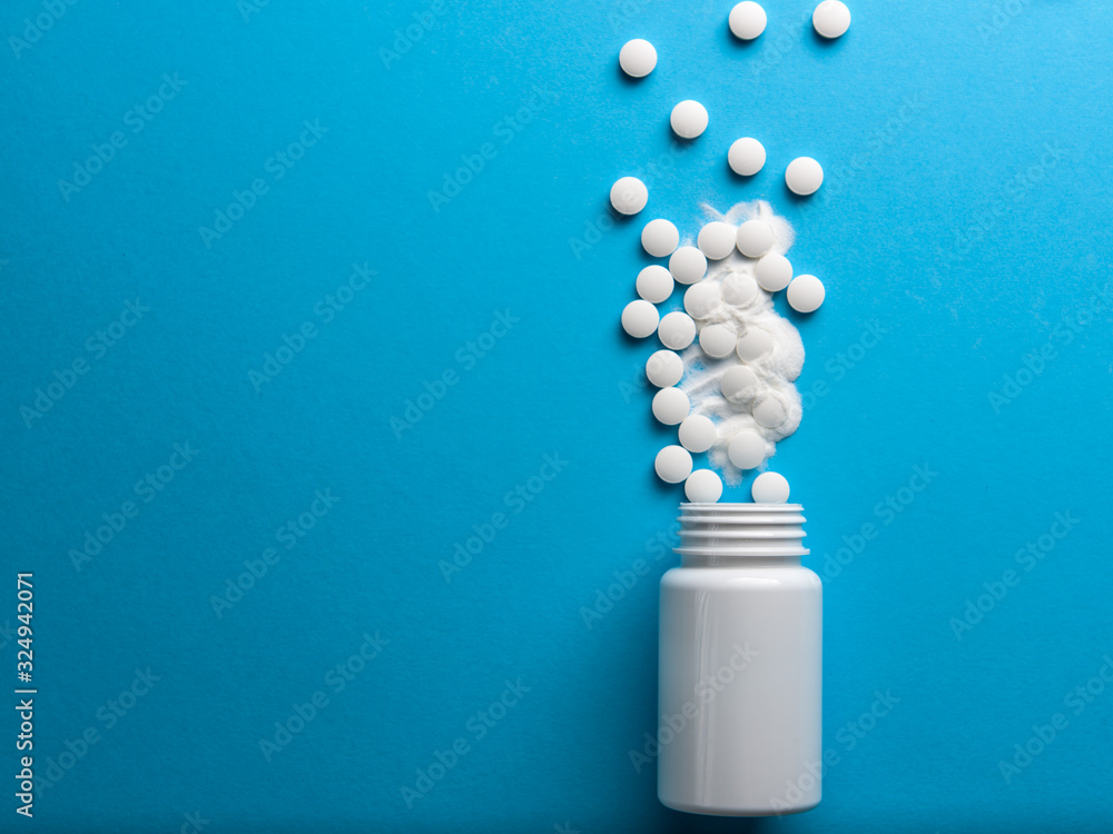White pills spilled from a white bottle on a blue background White pills spilled from a white bottle on a blue background