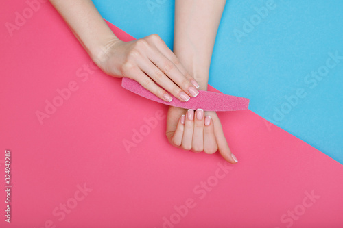 Beautiful female hands with stylish nail manicure gel polish on pink and blue background. Top view of manicure equipment. Woman files her nails. Free space for text.