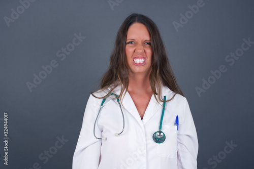 Mad crazy woman clenches teeth angrily  being annoyed with coming noise  dressed in fashionable clothes  isolated over gray background. Negative feeling concept.