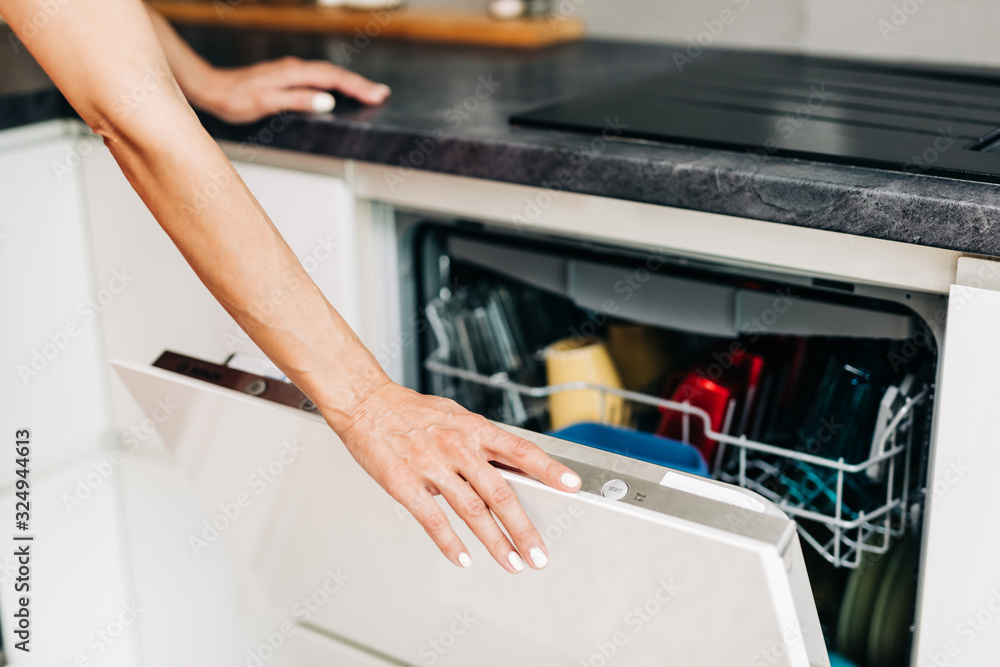 Woman's hand with an open dishwasher filled with clean dishes.. Woman's hand with an open dishwasher filled with clean dishes..