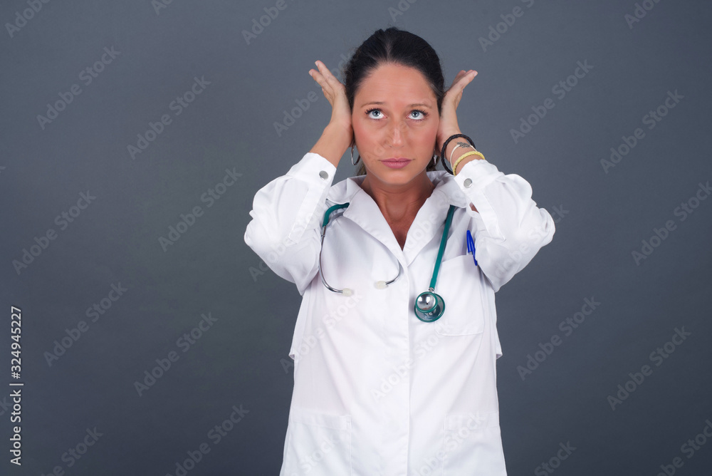 Doctor woman plugging ears with hands does not wanting to listen hard rock or loud music. European Young female ignoring noise or din covering her ears with hands avoiding loud sounds at street. Doctor woman plugging ears with hands does not wanting to listen hard rock or loud music. European Young female ignoring noise or din covering her ears with hands avoiding loud sounds at street.