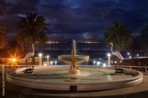 Eastern Beach Geelong fountain reserve overlooks the Corio Bay foreshore, This iconic 1930s art deco style Geelong fountain is surrounded by tall palms trees with a dramatic cloudy dusk sky background