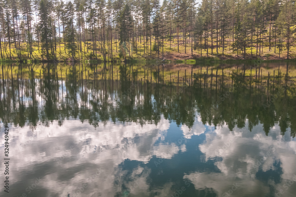 sky and tree reflection in secluded area by the lake. Calm waters and cloudy sky. fisherman in the background Sweden. selective focus. long exposure