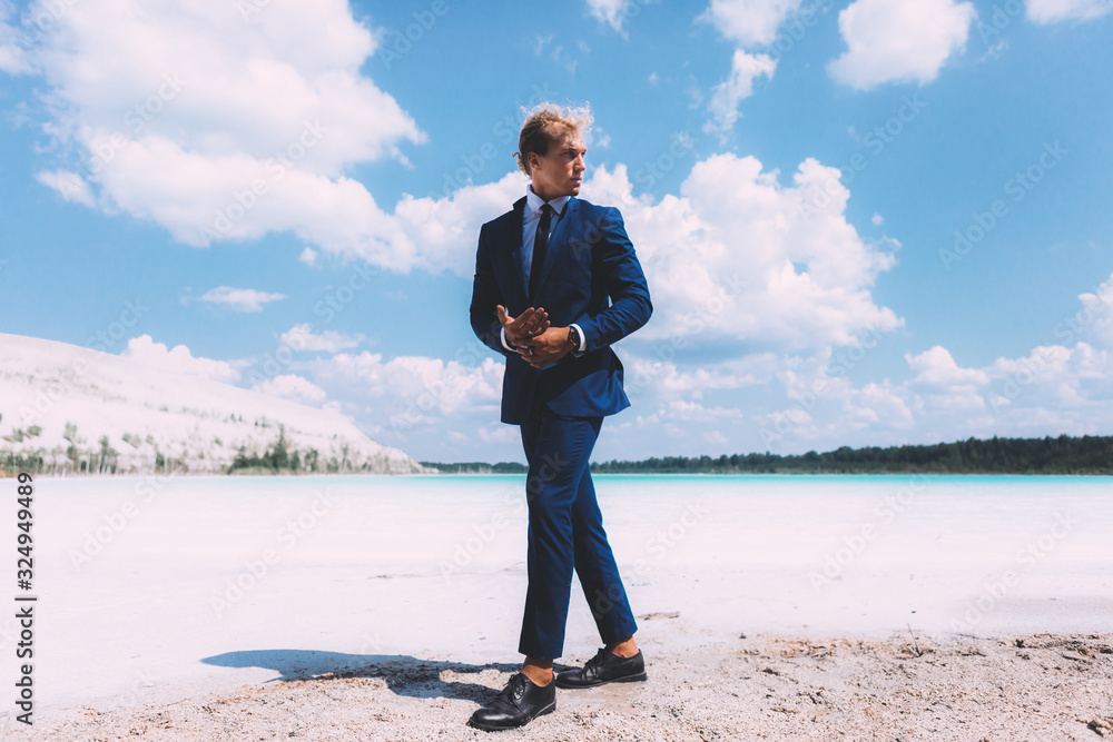 Blond curly man walking on the beach of crystal clear sea. Dressed business suit, blue color. Summer, trendy. Travel topic. Blond curly man walking on the beach of crystal clear sea. Dressed business suit, blue color. Summer, trendy. Travel topic.