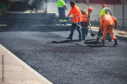 Asphalt paver machine and steam road roller during road construction and repairing works, process of asphalting and paving, workers working on the new road construction site, placing a layer