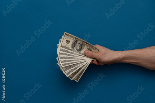 Hand holds money on a blue background.