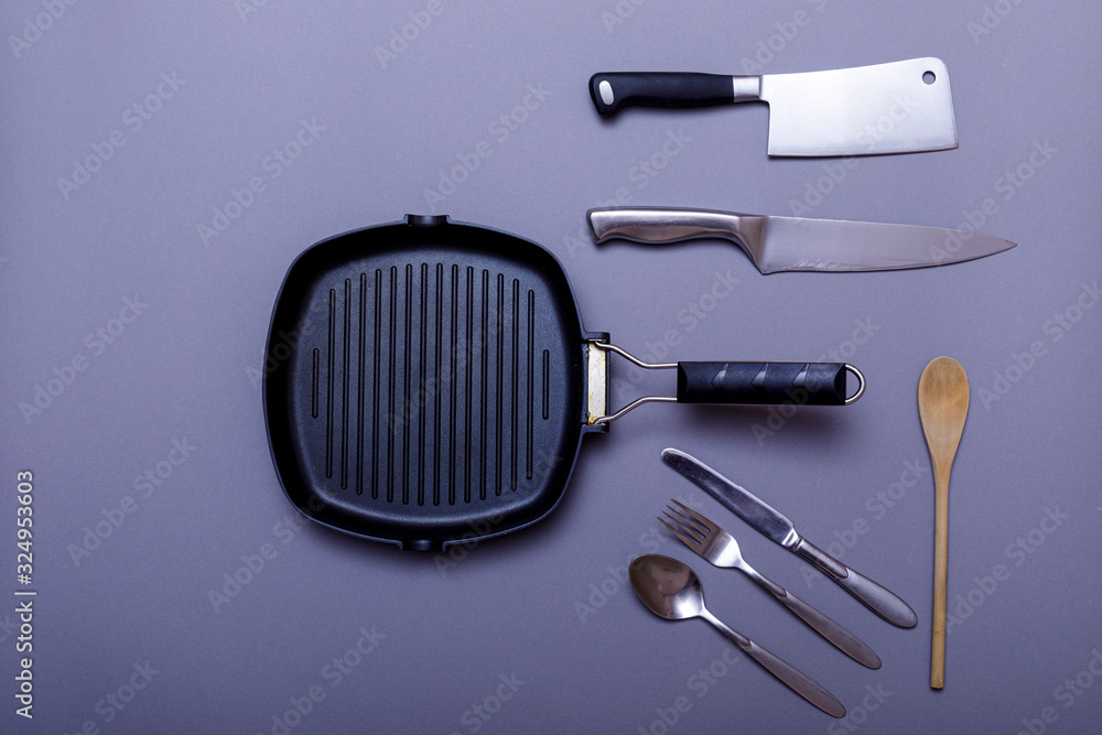 Fototapeta premium Metal knives with black on a grey table, grill pan, towel. Flat lay, layout with copy space.
