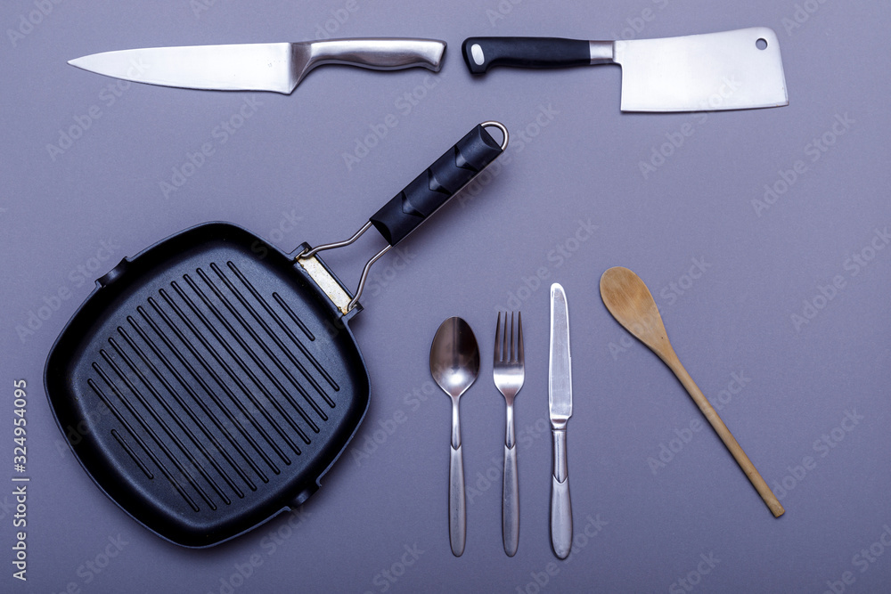 Metal knives with black on a grey table, grill pan, towel. Flat lay, layout with copy space. Metal knives with black on a grey table, grill pan, towel. Flat lay, layout with copy space.