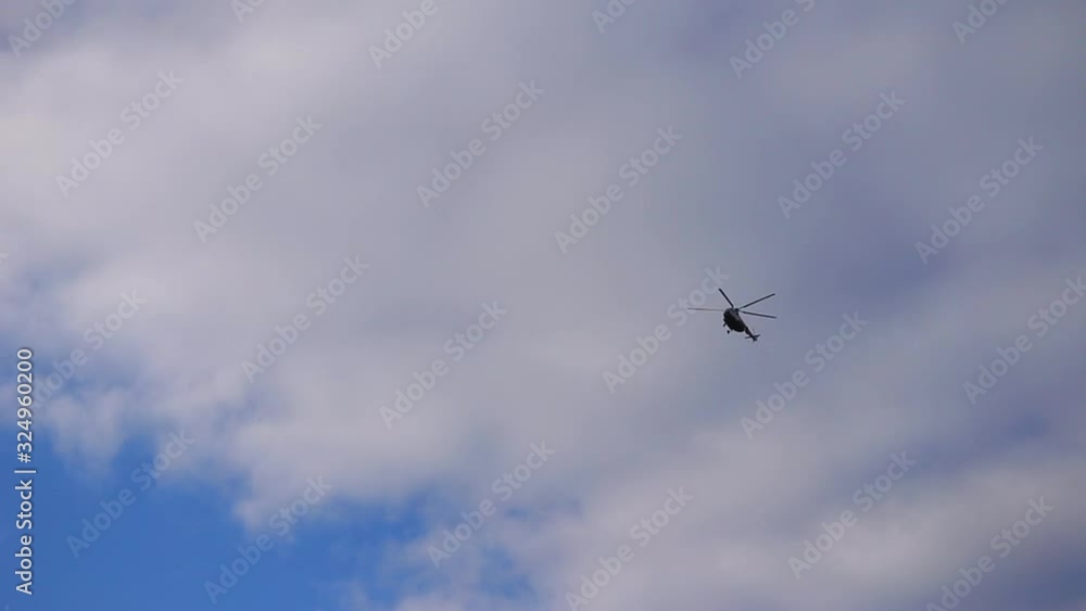 A helicopter fly across a deep blue sky. View through a silhouette of leafless tree branches on purple and white clouds background. A helicopter fly across a deep blue sky. View through a silhouette of leafless tree branches on purple and white clouds background.