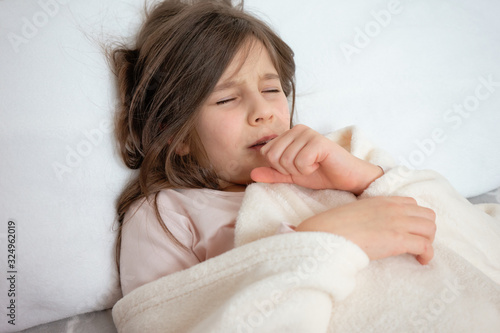 Little cute girl lies in bed and coughs violently with a cold, virus, gets sick