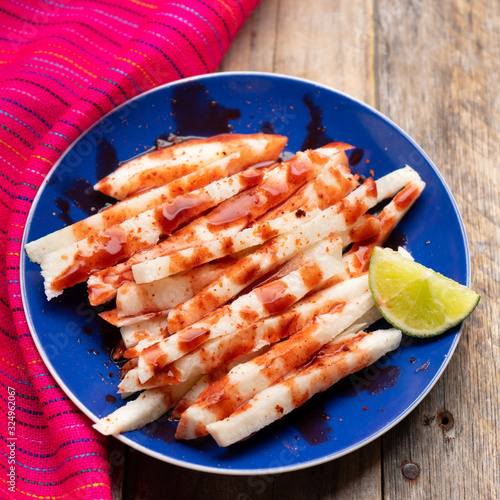 Mexican jicama  cutted with chili powder and piquant sauce on wooden background photo