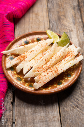 Mexican jicama  cutted with chili powder on wooden background photo