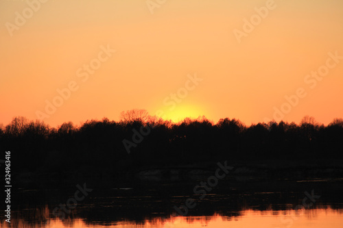 orange sunset behind the forest over the river in early spring