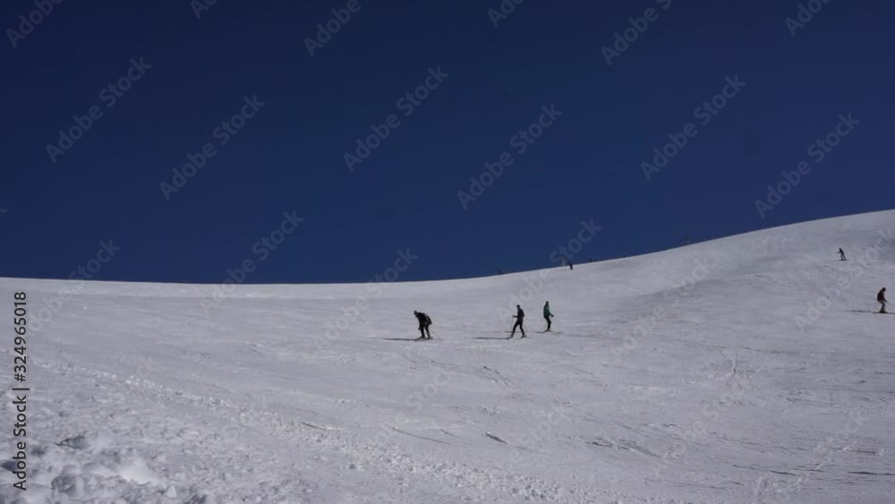 Amazing view of a snow capped hill with skiers and snowboarders riding downhill on a deep blue sky background. Ski resort in the snowy mountain woods on a bright winter day. Amazing view of a snow capped hill with skiers and snowboarders riding downhill on a deep blue sky background. Ski resort in the snowy mountain woods on a bright winter day.