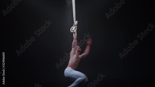 Muscular circus aerialist on the aerial straps in black studio photo