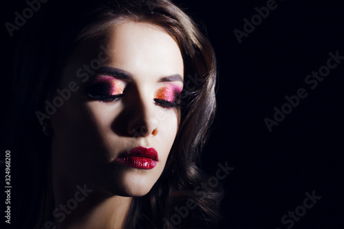 Portrait of a young luxurious woman in a low key. Bright makeup with scarlet lipstick, hairstyle with curls,
