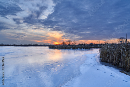Scenic View of Winter Lake Sunset with Blue Sky and Iced Over Lake with Cattails 