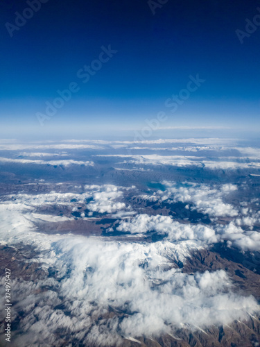 Beautiful photo from the birds view on clouds flying above high mountains peaks covered with snow