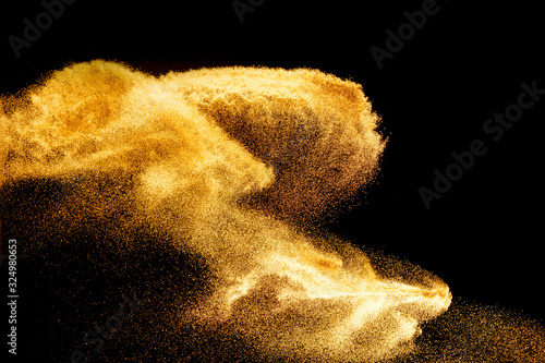 Golden sand explosion isolated on black background. Abstract sand cloud.Sandy fly wave in the air. photo