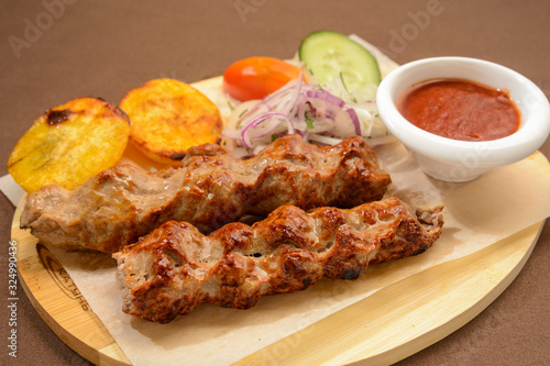 Kebab with fried potatoes, onion and vegetables on a wooden board.