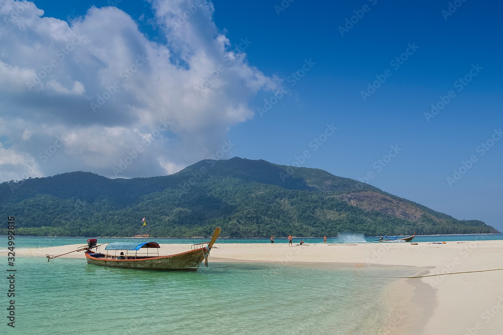 view seaside of a long-tail boat floating in blue-green sea around with white sand beach, green mountain and blue sky background, Lipe island, Satun, southern Thailand.