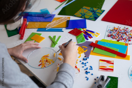 Woman puts out a mosaic of glass with tweezers, fusing, crafting