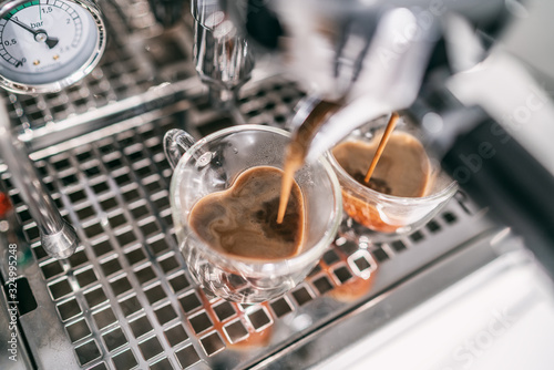 Coffee machine making two espresso cups in heart shape double wall glass macchiato mugs for lovers at cafe bar. photo