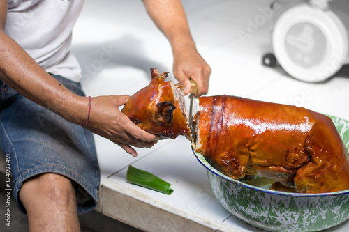 man hand cutting home pig suckling pork head with knife to be eaten after traditional hindu cultural sacrifice in bali, indonesia photo