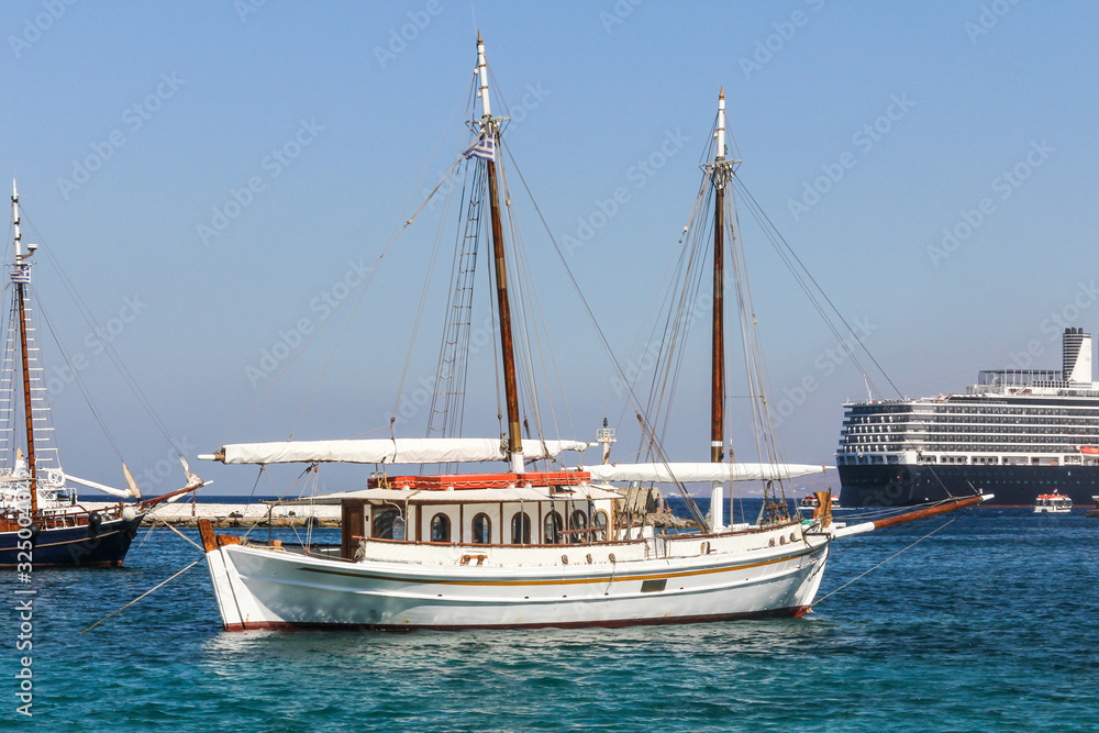 Typical Greek sailing yacht in Mykonos harbour, Greec with a cruise ship in the background