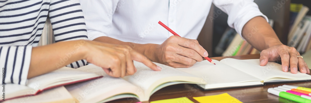 Young students classmates help friend catching up workbook and learning tutoring in a library, education and school concept