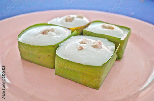 Abstract selective focus of tasty Thai jelly with taro ,creamy coconut topping recipe inside Pandan leaves cube calls Khanom Tako ,which is delicious sweet dessert like pudding with coconut topping photo