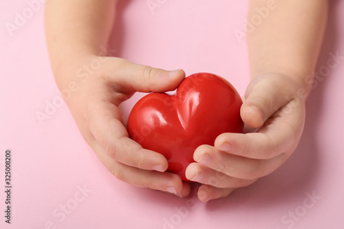 Child s hands with red heart on color background. Cardiology concept