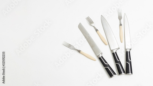 three forks, sharp kitchen knives with black handles isolated on white background. top view on group of tableware with shining metal blades. simple flat lay composition with copyspace. Space for text